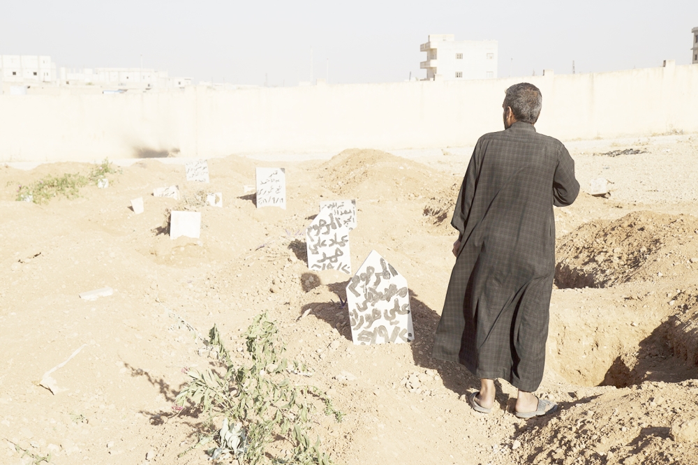 This picture released on Wednesday, Oct. 26, 2016 by the New York-based group Human Rights Watch, shows a family member stands next to the graves of three children who were killed when an explosive device planted by Islamic State group in a school detonated on September 27 in Manbij, Syria. Homemade landmines planted by the Islamic State group have killed and injured hundreds of civilians, including dozens of children, in the town of Manbij in northern Syria, Human Rights Watch says. (Ole Solvang, Human Rights Watch via AP)