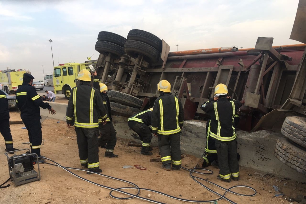 رجال الدفاع المدني خلال استخراج المحتجزين من تحت الصهريج المقلوب. (عكاظ)