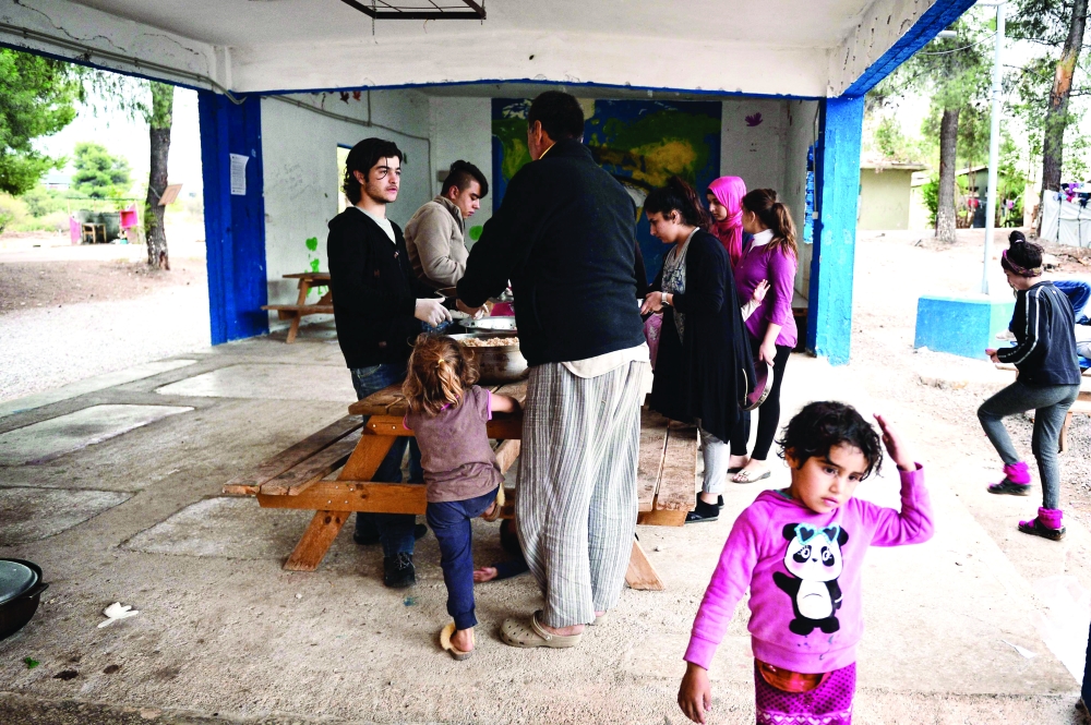 Refugees get meal cooked by chef Talal Rankoussi and volunteers outside the 'Cafe Rits' in Ritsona refugee camp, some 80 km north of Athens on December 21, 2016. Before braving a 'trip of death' to escape Syria, Talal Rankoussi was a chef in a Damascus restaurant considered the largest in the world.Bawabet Al Dimashq -- Damascus Gate -- still holds that distinction in the Guinness Book of Records as it can seat over 6,000 people.So when 41-year-old Talal was asked by a US benefactor to spice up the meals for several hundred fellow Syrians at the Ritsona camp near Athens, the two-decade culinary veteran did not hesitate. / AFP / LOUISA GOULIAMAKI
