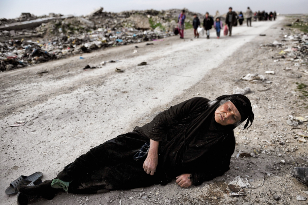 TOPSHOT - An Iraqi woman lies on the ground as civilians flee Mosul while Iraqi forces advance inside the city during fighting against Islamic State group's fighters on March 8, 2017.  Supported by US-led air strikes, the forces have made steady progress in their battle to seize Iraq's second city from the Islamic State group, announcing the recapture of two more areas. Hundreds of thousands of civilians are believed to still be trapped under jihadist rule in the Old City, where Abu Bakr al-Baghdadi proclaimed a 