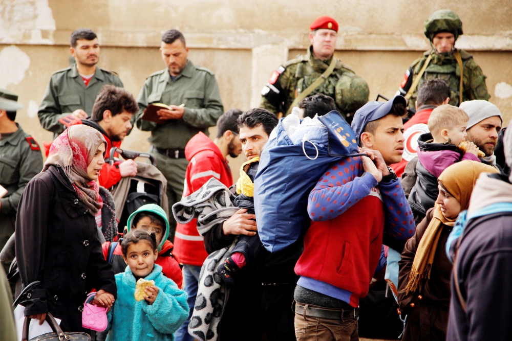 Syrian army soldiers (back L) and Russian soldiers (back R) monitor as rebel fighters and their families evacuate the besieged Waer district in the central Syrian city of Homs, after an agreement was reached between rebels and Syria's army, March 18, 2017. REUTERS/Omar Sanadiki