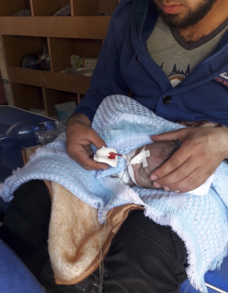 In this photo taken on Tuesday, April 4, 2017 and made available Wednesday, April 5, a Syrian man holds a suffering baby victim of alleged chemical weapons attacks in Syrian city of Idlib, inside Syria, near the Reyhanli border crossing, Turkey.  A suspected chemical attack in a town in Syria's rebel-held northern Idlib province killed dozens of people on Tuesday, opposition activists said, describing the attack as among the worst in the country's six-year civil war.(IHA via AP)