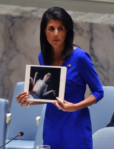 US Ambassador to the UN, Nikki Haley holds photos of victims as she speaks as the UN Security Council meets in an emergency session at the UN on April 5, 2017, about the suspected deadly chemical attack that killed civilians, including children, in Syria. / AFP / TIMOTHY A. CLARY
