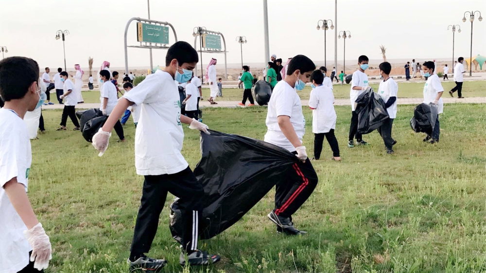 طلاب مشاركون في المبادرة خلال تنظيفهم أحد المنتزهات في تيماء.  (عكاظ)