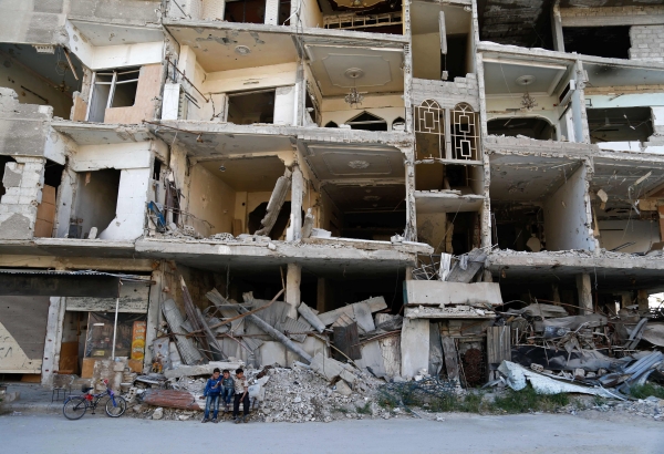 TOPSHOT - Syrian children sit in front of a heavily damaged building in the rebel-held town of Erbin in the eastern Ghouta region on the outskirts of the Syrian capital Damascus, on April 24, 2017. / AFP / ABDULMONAM EASSA
