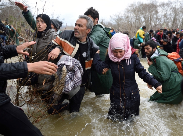 (FILES) This file photo taken on March 14, 2016 shows refugees and migrants trying to cross a river on their way to Macedonia from a makeshift camp at the Greek-Macedonian border, near the Greek village of Idomeni, where thousands of refugees and migrants are stranded by the Balkan border blockade. An exhibition showcasing this image and other work of Agence France-Presse photographers who have documented the hope and heartbreak of Europe's migration crisis opened in Brussels on May 3, 2017. The show at the Bozar arts centre, titled 