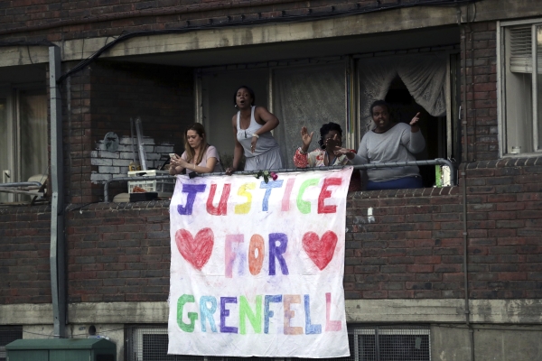 People watch from a balcony as people walk during a demonstration following the fire at Grenfell Towers that engulfed the 24-storey building on Wednesday morning, in London, Friday June 16, 2017. Grief over a London high-rise tower fire that killed dozens turned to outrage Friday amid reports that the materials used in a recent renovation of the public housing block may have fueled the inferno. (AP Photo/Tim Ireland)