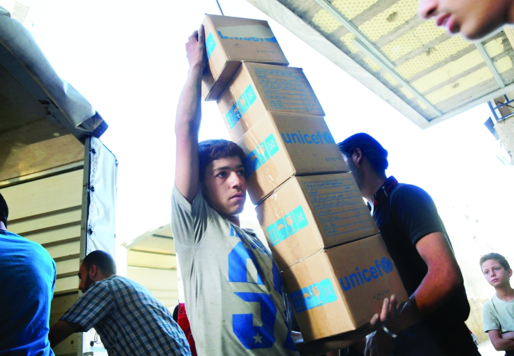 A Syrian youth carries boxes of aid donated by UNICEF in the rebel held and besieged town of Harasta, in the Eastern Ghouta region outside Damascus, on Jun 19, 2017. The United Nations estimates more than 600,000 people in Syria are living under siege, a tactic employed primarily by government forces, but also used by rebel fighters and the Islamic State group. / AFP / AMER ALMOHIBANY
