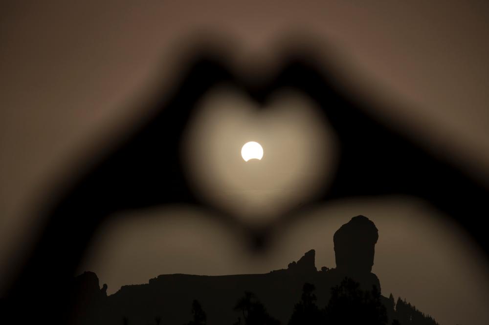 A woman makes a heart shape with her hands during a partial eclipse of the sun over the 