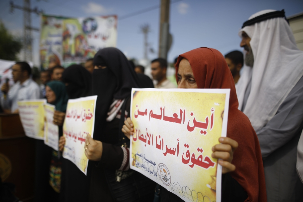 Palestinians block the road ahead of a convoy transporting United Nations Secretary General Antonio Guterres, upon his arrival at Erez border crossing in Beit Hanun, in the northern Gaza Strip, on August 30, 2017. Arabic writing on placards reads: «Where is the world from the rights of our heroic prisoners?» / AFP / MOHAMMED ABED
