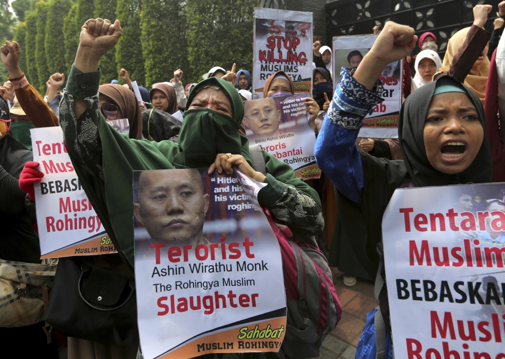 Muslim women, one of them holding a poster depicting Wirathu, the leader of Myanmar's nationalist Buddhist monks, raise their fists as they shout slogans during a rally against persecution of Rohingya Muslim minority, outside Myanmar Embassy in Jakarta, Indonesia, Monday, Sept. 4, 2017. Hundreds of Muslim women staged the rally in the third day of protests calling for the government of the world's most populous Muslim country to take a tougher stance against persecution of the Rohingya, an oppressed Muslim minority in overwhelmingly Buddhist Myanmar. (AP Photo/Tatan Syuflana)