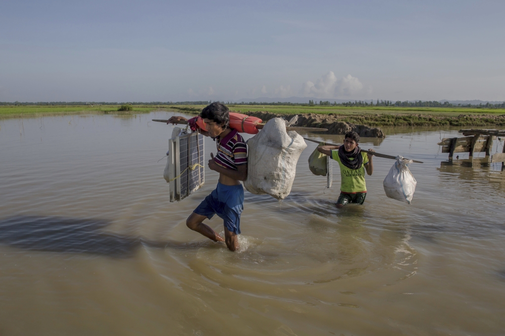 A Rohingya Muslim man Nur Karim, left, and his cousin Khair Mohammad carry their belongings while walking past a channel of the Naf River after crossing over from Myanmar into Bangladesh, at Teknaf, Bangladesh, Friday, Sept. 22, 2017. Karim walked through forests for five days before a boat helped him cross the dangerous waters of the rain-flooded river to be reunited with his mother, who had crossed over two weeks ago with his sister's family. But his relief was tinged by a deep pain. In the chaos of their escape, as Myanmar soldiers fired at them, he got separated from his wife and child. (AP Photo/Dar Yasin)