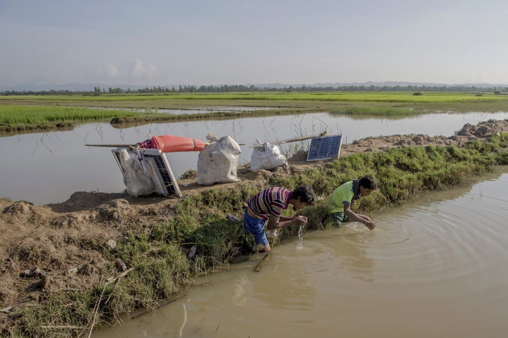 A Rohingya Muslim Nur Karim, left, and his cousin Khair Mohammad drink water from a channel of the Naf river after crossing over from Myanmar into Bangladesh, at Teknaf, Bangladesh, Friday, Sept. 22, 2017. Karim walked through forests for five days before a boat helped him cross the dangerous waters of the rain-flooded Naf river to Bangladesh to be reunited with his mother, who had crossed over two weeks ago with his sister's family. But his relief was tinged by a deep pain. In the chaos of their escape, as Myanmar soldiers fired at them, he got separated from his wife and child. (AP Photo/Dar Yasin)