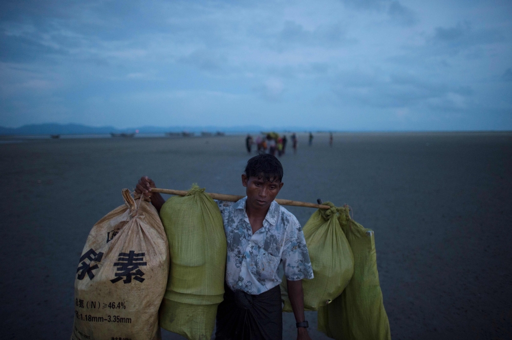 TOPSHOT - A Rohingya Muslim refugee carries his belongings as he walks with other people by night after crossing the border from Myanmar, on the Bangladeshi shores of the Naf river in Teknaf on September 29, 2017. More than half a million Rohingya Muslims have poured into Bangladesh in the last month, fleeing a vicious Myanmar military crackdown on Rohingya rebels that has gutted villages across northern Rakhine state. Scores have drowned while trying to cross waters separating the two countries, while those who survive face new dangers as they cram into squalid refugee settlements where food and clean water are in short supply. / AFP / FRED DUFOUR 