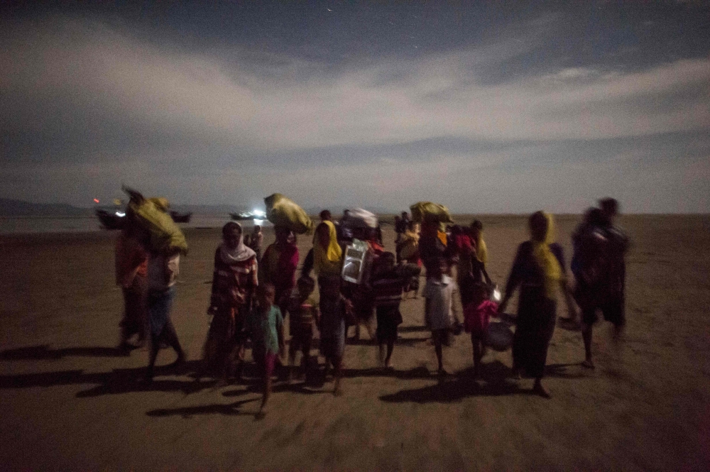 TOPSHOT - Rohingya Muslim refugees walk by night after crossing the border from Myanmar, on the Bangladeshi shores of the Naf river in Teknaf on September 29, 2017. More than half a million Rohingya Muslims have poured into Bangladesh in the last month, fleeing a vicious Myanmar military crackdown on Rohingya rebels that has gutted villages across northern Rakhine state. Scores have drowned while trying to cross waters separating the two countries, while those who survive face new dangers as they cram into squalid refugee settlements where food and clean water are in short supply. / AFP / FRED DUFOUR 