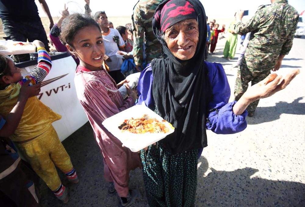 An Iraqi woman receives food from a charity in a village on the outskirts of Hawija on October 6, 2017, a day after Iraqi forces retook the northern city from Islamic State (IS) group fighters. / AFP / AHMAD AL-RUBAYE