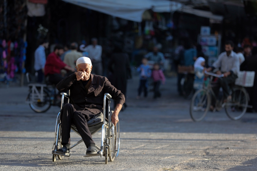 A elderly Syrian man on a wheelchair makes his way at a street in Douma, a rebel-held town on the outskirts of the capital Damascus, on October 24, 2017. 

 According to the World Bank, the conflict in Syria has cost the country's economy some $226 billion -- about four times the country's gross domestic product in 2010. The fighting has damaged or destroyed 27 percent of Syria's housing stock and about half the country's medical and educational facilities. About 85 percent of the population lives below the poverty line and half are unemployed. 
 / AFP / Amer ALMOHIBANY
