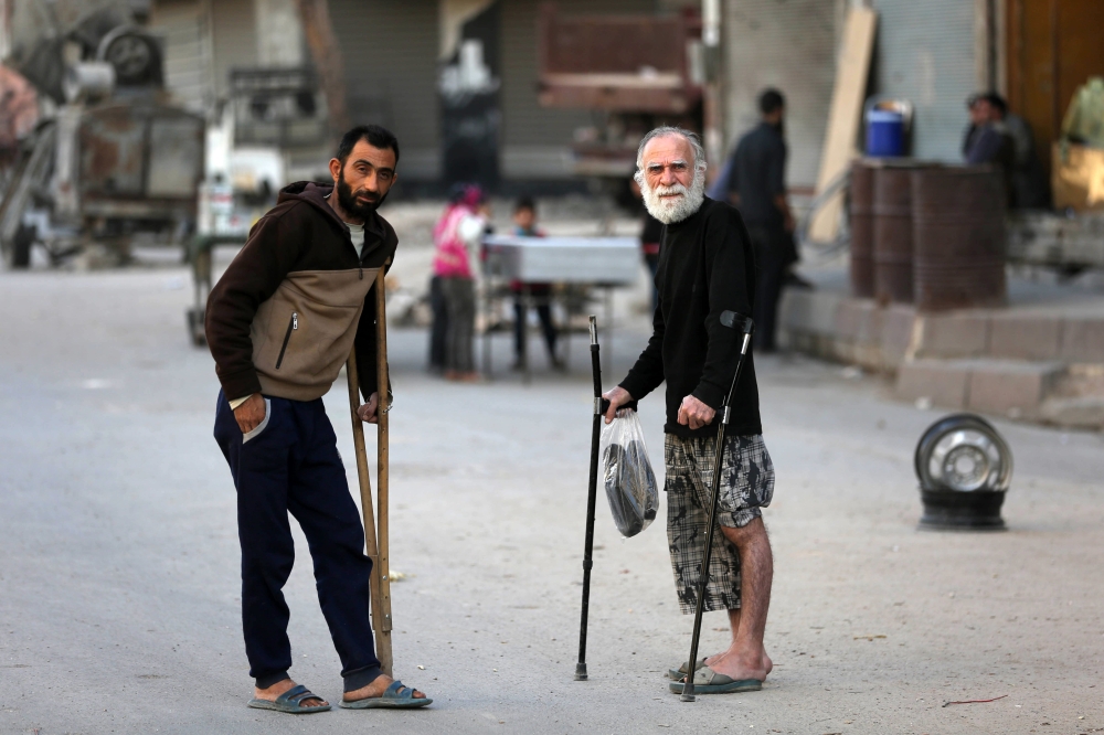 Syrian men using crutches stand at a street in Douma, a rebel-held town on the outskirts of the capital Damascus, on October 24, 2017. 

 According to the World Bank, the conflict in Syria has cost the country's economy some $226 billion -- about four times the country's gross domestic product in 2010. The fighting has damaged or destroyed 27 percent of Syria's housing stock and about half the country's medical and educational facilities. About 85 percent of the population lives below the poverty line and half are unemployed. 
 / AFP / Amer ALMOHIBANY
