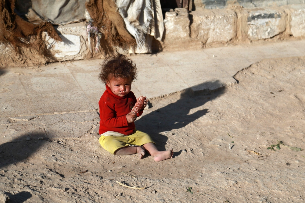 A displaced Syrian child eats an ear of corn as she sits on the floor in a heavily damaged area where her family took refuge in the rebel-held town of Saqba, in Eastern Ghouta on October 24, 2017. / AFP / ABDULMONAM EASSA
