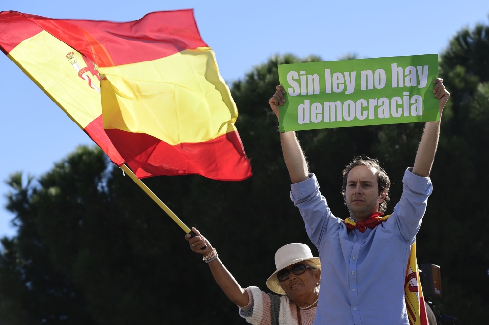 A woman waves a Spanish flag behind a man holding a sign reading 