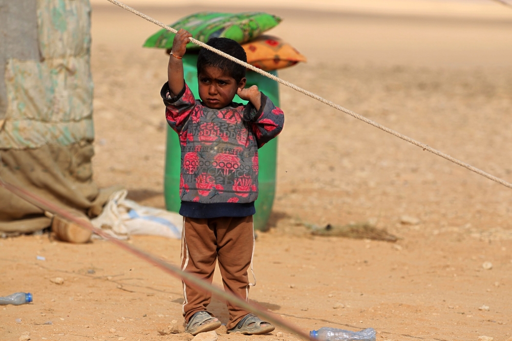 An Iraqi child, displaced from the city of al-Qaim, stands outside a tent near al-Qaim, in western Anbar province, on the Syrian border on November 2, 2017. / AFP / AHMAD AL-RUBAYE
