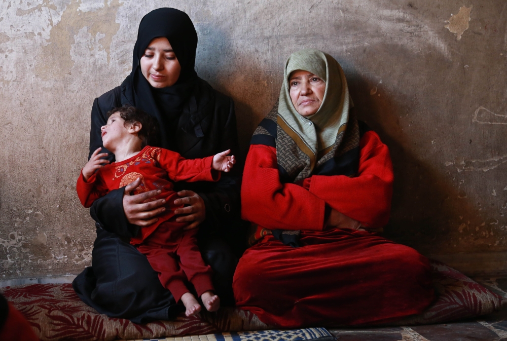 A woman holds her one-year-old son Qamar who is suffering from malnutrition as members of the family of Umm Saeed gather in their house on November 6, 2017 in Saqba, in the besieged rebel-held Eastern Ghouta area near Damascus, where residents and relief groups have warned a humanitarian crisis is escalating. Eastern Ghouta was once a prime agricultural region famed for its orchards, but the rebel stronghold has been under a tight government siege since 2013, causing shortages of food and medicine.
 / AFP / ABDULMONAM EASSA
