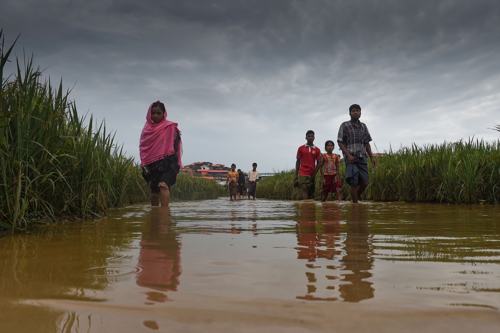 TOPSHOT - Rohingya refugees walk through water at Thankhali refugee camp in the Bangladeshi district of Ukhia on November 17, 2017. An estimated 618,000 Muslim Rohingya have fled mainly Buddhist Myanmar since a military crackdown was launched in Rakhine in August triggered an exodus, straining resources in the impoverished country. / AFP / Munir UZ ZAMAN
