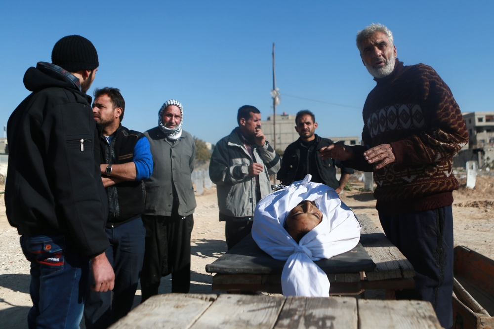 Syrian men mourn over the body of a victim during his funeral following a reported air strike in the rebel-held besieged town of Arbin, in the Eastern Ghouta region on the outskirts of Damascus, on December 2, 2017. / AFP / ABDULMONAM EASSA
