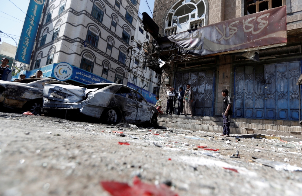 People stand next to damaged cars on a street where Houthi fighters recently clashed with forces loyal to Yemen's former president Ali Abdullah Saleh in Sanaa, Yemen December 5, 2017. REUTERS/Khaled Abdullah