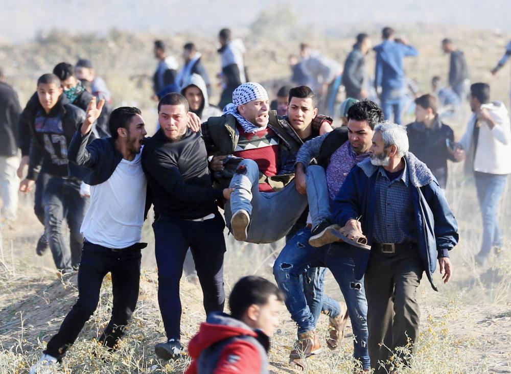 Palestinian protesters carry a wounded comrade during clashes with Israeli forces on December 8, 2017 near the border fence with Israel, east of Gaza City.  Palestinians clashed with Israeli security forces after calls for a 