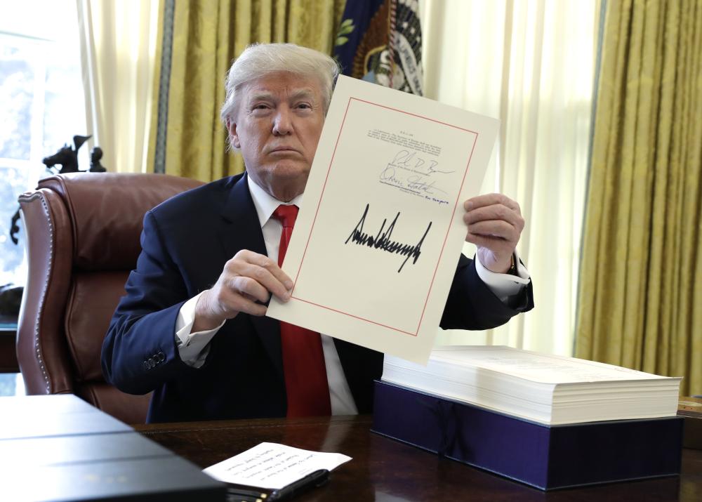 President Donald Trump displays the $1.5 trillion tax overhaul package he had just signed, Friday, Dec. 22, 2017, in the Oval Office of the White House in Washington. Trump touted the size of the tax cut, declaring to reporters in the Oval Office before he signed it Friday that 