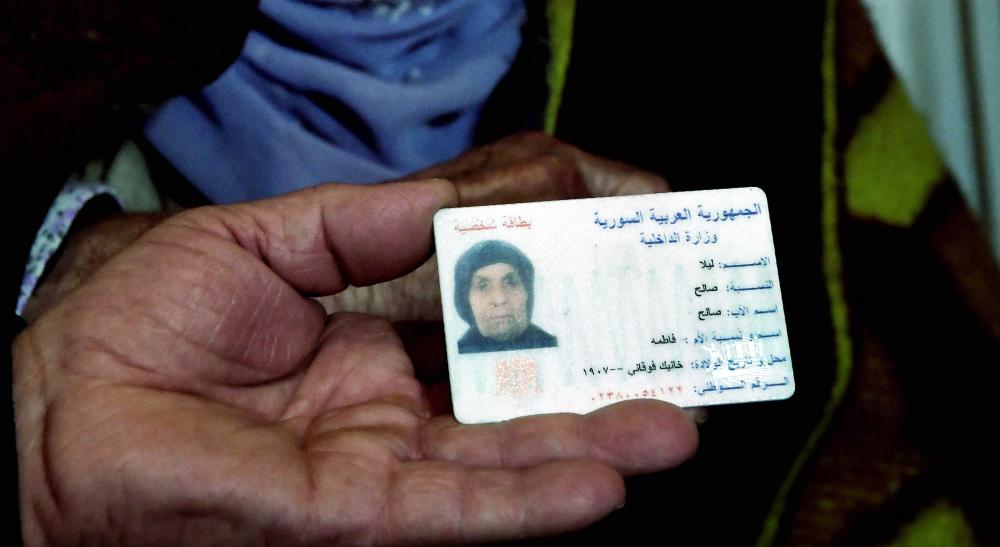 A relative shows ID papers of Laila Saleh (rear C), a 110 years old Syrian refugee from Kobane, as she sits on the floor surrounded by members of her family, in an appartement in Athens, on December 15, 2017. Laila Saleh, who was born in Kobane on 1907, also made the dangerous crossing of the Aegean sea with an inflatable boat. She hopes to see again her granddaughter Nasrin, a refugee who found shelter in Germany. Laila Saleh arrived on the Greek island of Lesbos in early November with her grandson Halil, her youngest son Ahmad, Halil's father, her daughter-in-law, and Halil's wife and their two children. / AFP / ARIS MESSINIS
