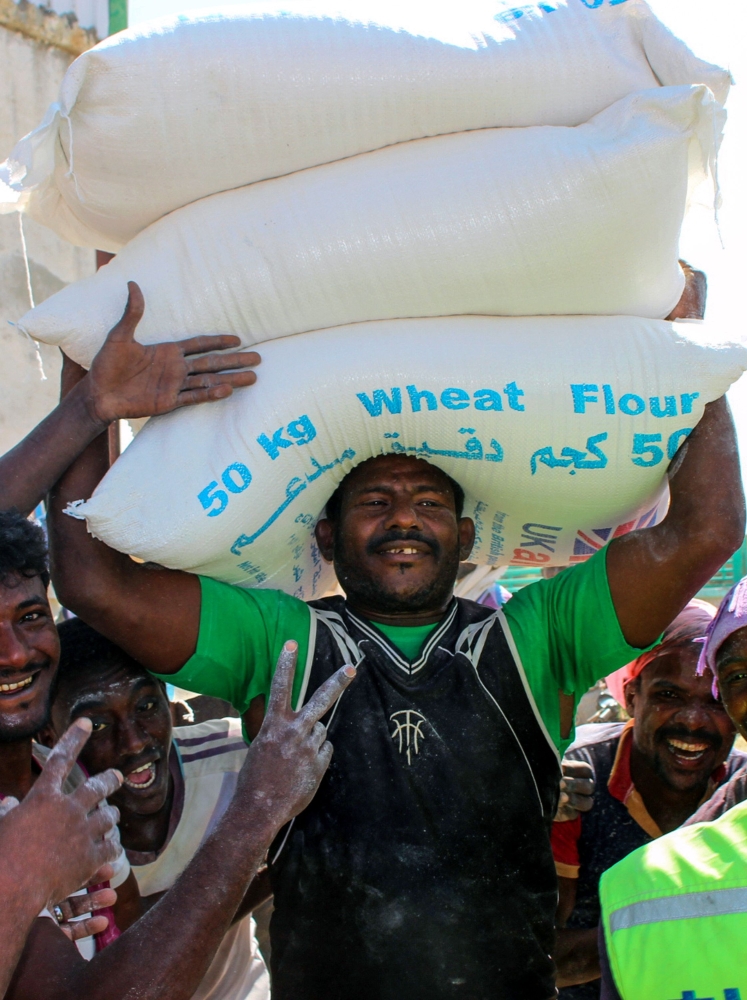 A Yemeni man carries sacks of wheat distributed as food aid by a local charity at a camp for the displaced, in the northern province of Hajjah on December 23, 2017.  / AFP / STRINGER
