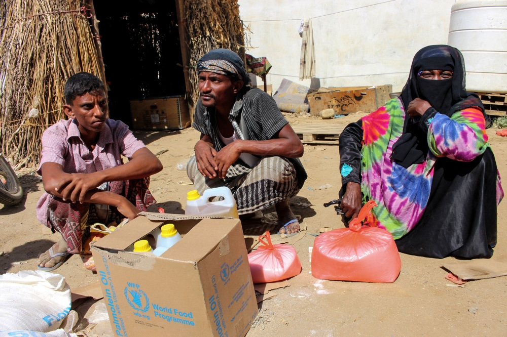 A Yemeni man, woman, and youth sit next to food supplies distributed by a local charity at a camp for the displaced, in the northern province of Hajjah on December 23, 2017.  / AFP / STRINGER
