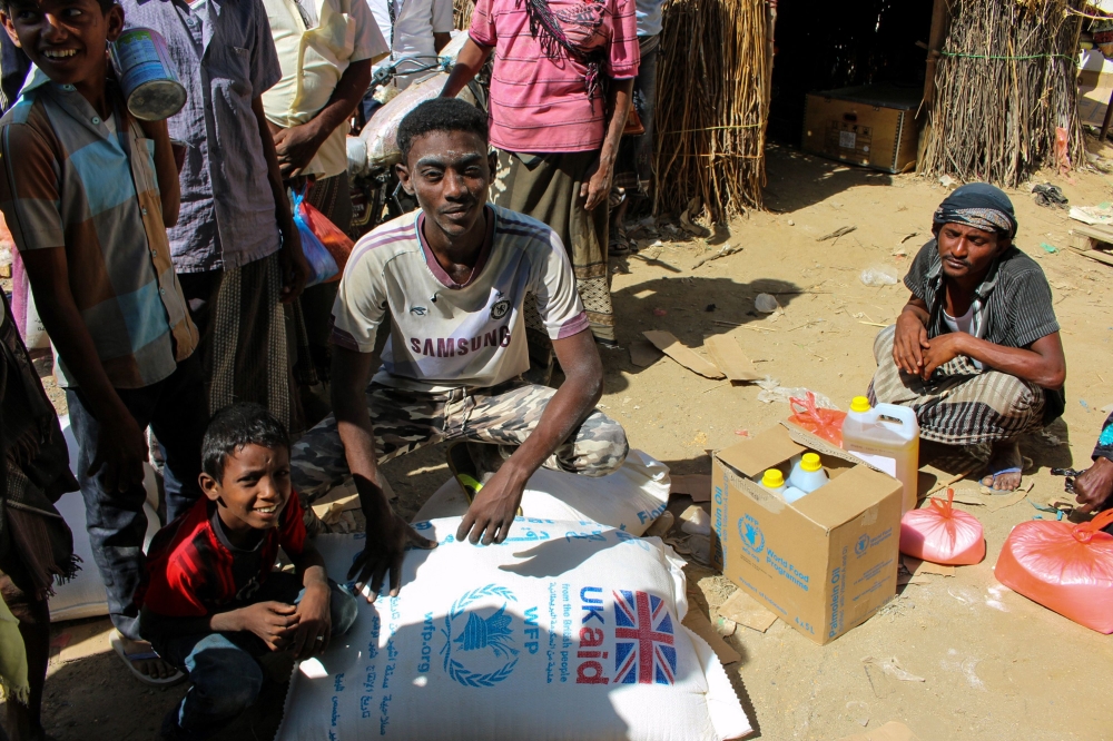 A Yemeni man sits next to sacks of wheat and containers of cooking oil distributed as food aid by a local charity at a camp for the displaced, in the northern province of Hajjah on December 23, 2017.  / AFP / STRINGER
