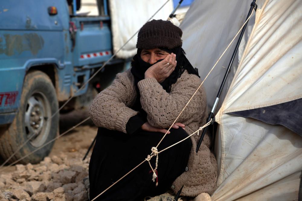 A displaced Syrian woman, who was forced to leave her hometown by the war against the Islamic State (IS) group, sits next to a tent at the Ain Issa camp on December 18, 2017.     As temperatures drop, tens of thousands of civilians forced out of their homes by Syria's war are spending yet another winter in flimsy plastic tents or abandoned half-finished buildings. And without heating, blankets and warm clothes, or access to proper medical care, even a simple cold can turn deadly. / AFP / Delil souleiman
