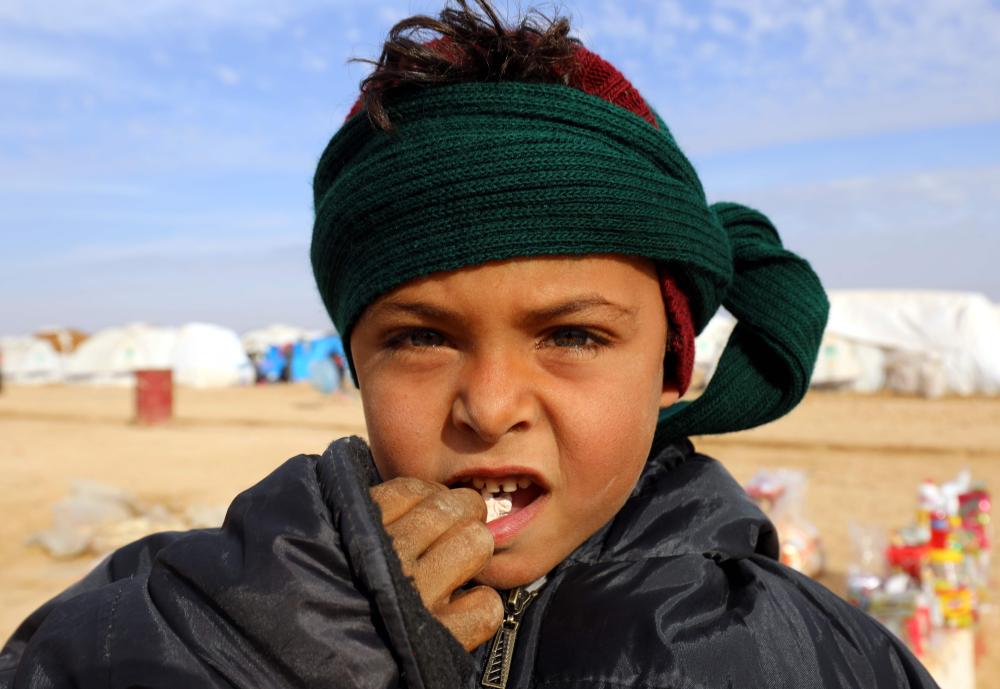 A displaced Syrian child, who was forced to leave his hometown by the war against the Islamic State (IS) group, looks into the camera at the Ain Issa camp on December 18, 2017.     As temperatures drop, tens of thousands of civilians forced out of their homes by Syria's war are spending yet another winter in flimsy plastic tents or abandoned half-finished buildings. And without heating, blankets and warm clothes, or access to proper medical care, even a simple cold can turn deadly. / AFP / Delil souleiman
