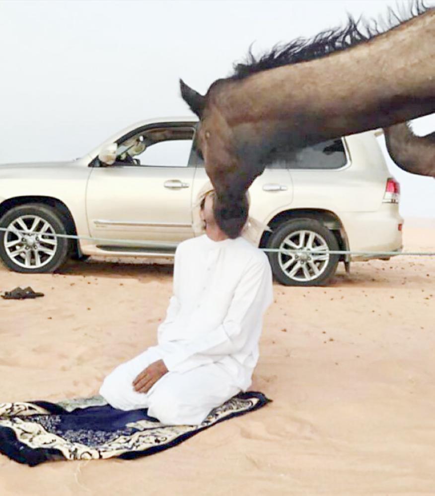 



مالك الإبل حمد بن شامان في لقطة نادرة مع إحدى نياقه في صحراء الربع الخالي.  (عكاظ)  