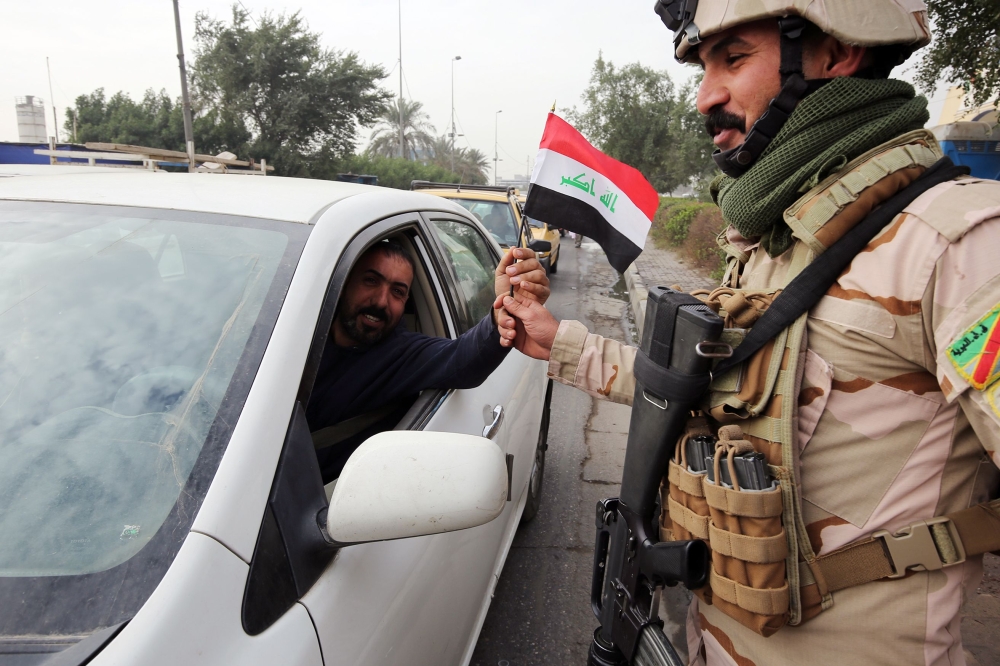 An Iraqi man gives a soldier a national flag at a checkpoint in the capital Baghdad on January 6, 2018, during festivities marking Iraq's Army Day. / AFP / SABAH ARAR
