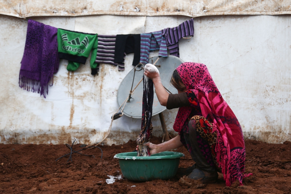 A displaced Syrian woman from Idlib province washes clothes at a makeshift camp near the rebel-held town of Azaz in northern Syria on January 6, 2018.  / AFP / Nazeer al-Khatib
