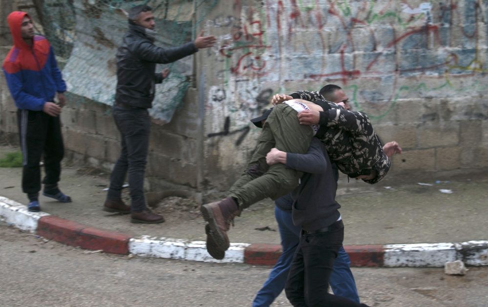 Palestinian youths evacuate a wounded comrade during clashes with Israeli forces in Jenin, in the north of the occupied West Bank, on January 18, 2018.  A Palestinian was killed during clashes with Israeli forces in Jenin, the Palestinian health ministry announced. Israel's Shin Beth security services said shots were fired during a raid by border guards to capture the alleged perpetrators of an attack earlier this month in which a rabbi was shot dead.
 / AFP / JAAFAR ASHTIYEH
