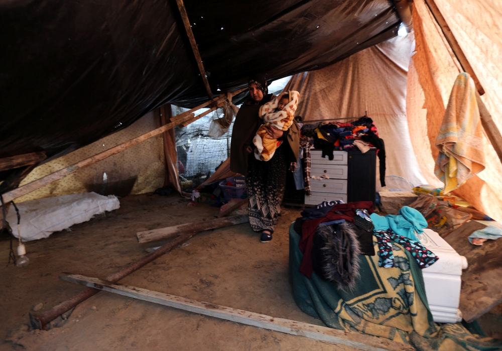 A Palestinian woman holds a baby inside a tent on a rainy day in Rafah in the southern Gaza Strip January 19, 2018. REUTERS/Ibraheem Abu Mustafa