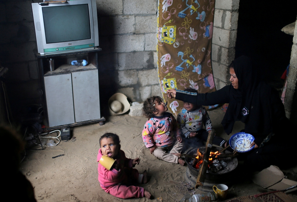 A Palestinian woman feeds her daughter as they sit by a fire on a rainy day in Khan Younis in the southern Gaza Strip January 19, 2018. REUTERS/Ibraheem Abu Mustafa     TPX IMAGES OF THE DAY