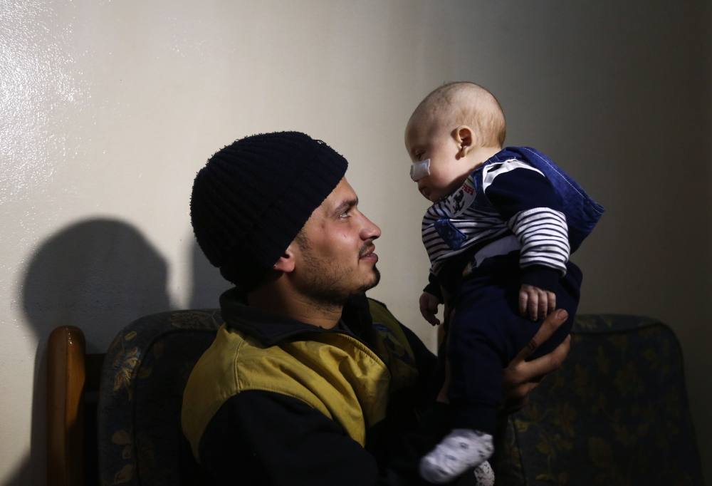 TOPSHOT - Twenty-seven-year-old member of the White Helmets rescue forces, Saeed al-Masri, holds his three-month-old son Yehya who he rescued after bombardment hit their home the previous week in Saqba in Syria's rebel-held Eastern Ghouta area on February 12, 2018. 
 For years, Samir Salim and his brothers rescued neighbours and relatives pinned underground after bombardment on Syria's rebel-held Eastern Ghouta. But last week, they could not save their own mother. / AFP / ABDULMONAM EASSA
