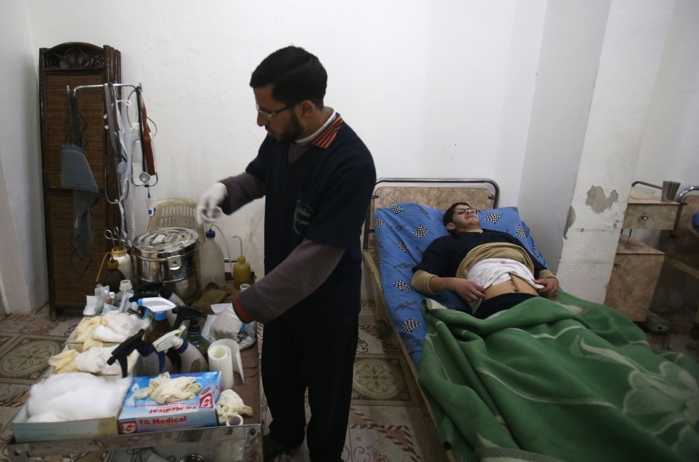 Malek Abu Jaber (R), a 20-year-old nurse, lies on a bed as a colleague changes his bandages at a makeshift clinic in the rebel-held town of Jisreen, in the besieged Eastern Ghouta region on the outskirts of the capital Damascus, on February 10, 2018, after he was injured on his way home earlier by an air strike. Eastern Ghouta, the last rebel bastion on the capital's doorstep, is home to around 400,000 besieged Syrians.  
In early February 2018, Syrian warplanes and artillery conducted an intense five-day campaign there that left around 250 civilians dead and triple that number wounded. / AFP / ABDULMONAM EASSA
