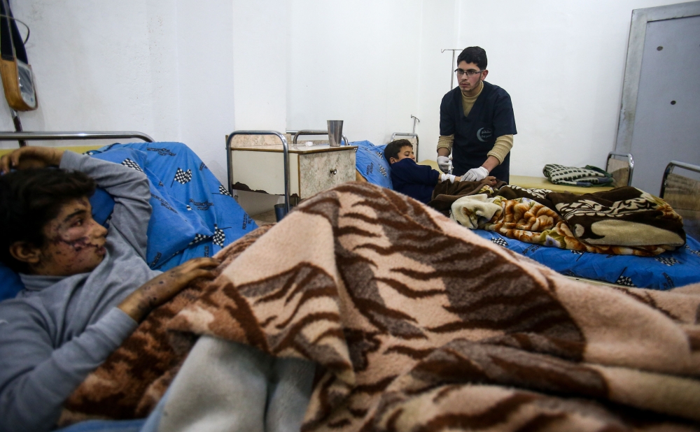 Malek Abu Jaber, a 20-year-old nurse, tends to injured Syrian children at a makeshift clinic in the rebel-held town of Jisreen, in the besieged Eastern Ghouta region on the outskirts of the capital Damascus, on February 10, 2018, after he was injured on his way home earlier by an air strike. Eastern Ghouta, the last rebel bastion on the capital's doorstep, is home to around 400,000 besieged Syrians.  
In early February 2018, Syrian warplanes and artillery conducted an intense five-day campaign there that left around 250 civilians dead and triple that number wounded. / AFP / ABDULMONAM EASSA
