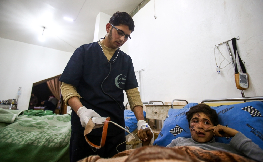 Malek Abu Jaber, a 20-year-old nurse, tends to injured Syrian children at a makeshift clinic in the rebel-held town of Jisreen, in the besieged Eastern Ghouta region on the outskirts of the capital Damascus, on February 10, 2018, after he was injured on his way home earlier by an air strike. Eastern Ghouta, the last rebel bastion on the capital's doorstep, is home to around 400,000 besieged Syrians.  
In early February 2018, Syrian warplanes and artillery conducted an intense five-day campaign there that left around 250 civilians dead and triple that number wounded. / AFP / ABDULMONAM EASSA
