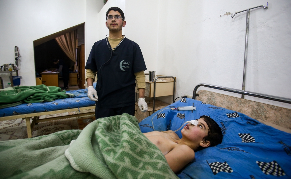 Malek Abu Jaber, a 20-year-old nurse, tends to injured Syrian children at a makeshift clinic in the rebel-held town of Jisreen, in the besieged Eastern Ghouta region on the outskirts of the capital Damascus, on February 10, 2018, after he was injured on his way home earlier by an air strike. Eastern Ghouta, the last rebel bastion on the capital's doorstep, is home to around 400,000 besieged Syrians.  
In early February 2018, Syrian warplanes and artillery conducted an intense five-day campaign there that left around 250 civilians dead and triple that number wounded. / AFP / ABDULMONAM EASSA
