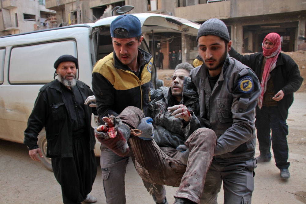 EDITORS NOTE: Graphic content / TOPSHOT - Civil Defence volunteers, known as the White Helmets, carry a wounded man into a makeshift hospital in the rebel-held town of Douma, following air strikes by regime forces on the besieged Eastern Ghouta region on the outskirts of the capital Damascus on February 20, 2018. Regime air strikes have pushed the death toll from three days of bombing in Syria's rebel Ghouta to over 200 as Damascus pitched pro-government forces into the fray against Turkey in a Kurdish-held border region. Held by rebels since 2012, Eastern Ghouta is the last opposition pocket around Damascus and President Bashar al-Assad is keen to retake it with an apparently imminent ground assault.
 / AFP / Hamza Al-Ajweh
