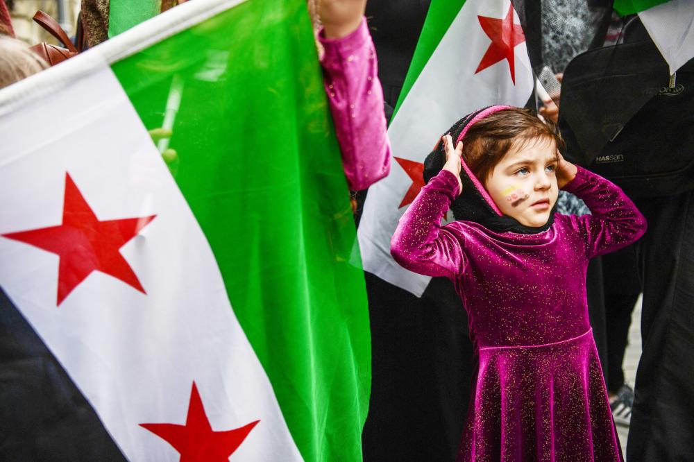 A girl reacts as she stands next to a protester holding a Syrian former independence flag (which have been adopted by forces fighting against Syrian pro-government forces in Syria) in front of Russian Consulate in Istanbul on February 22, 2018 during a protest against the airstrikes and shelling by the Syrian government forces in Ghouta. The Syrian regime rained rockets and bombs on Eastern Ghouta on February 22, killing another 19 civilians as international pressure mounted to stop the carnage in the rebel-held enclave. / AFP / OZAN KOSE
